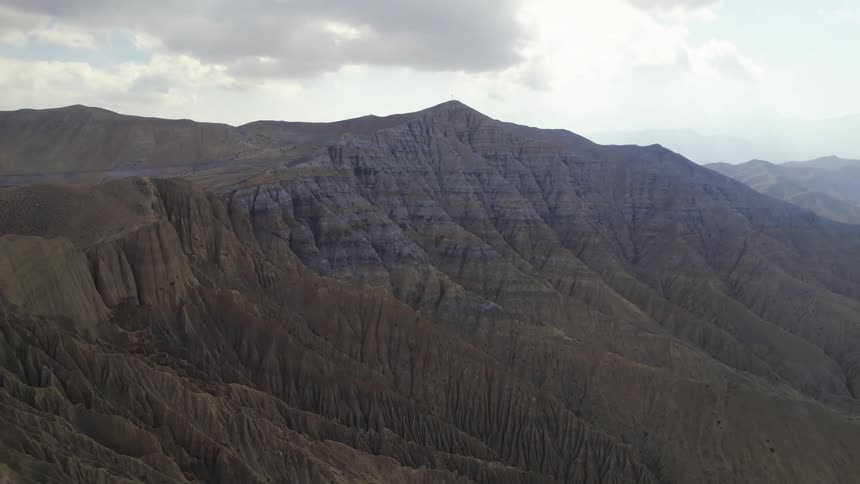 An aerial of a large mountain region with ridges along the mountain side on a bright day