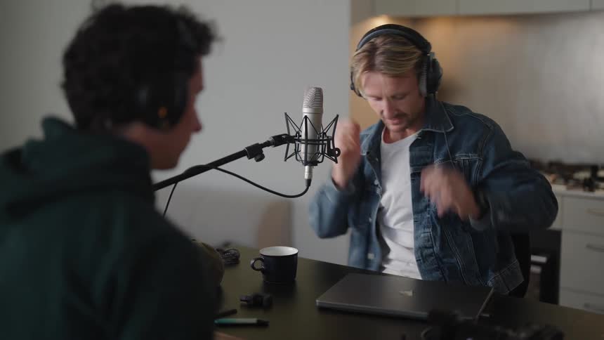 Two people adjusting headphones and other electronics on a podcast