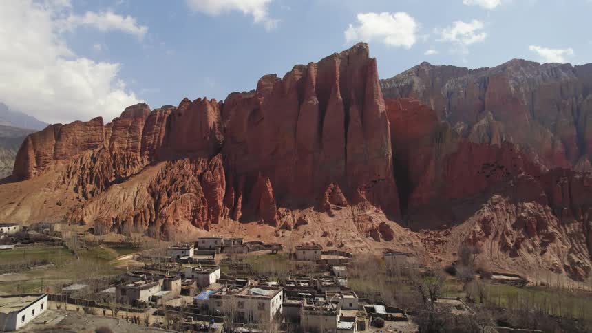 An aerial of tall mountain cliffs with a rural village at the bottom in a plateau