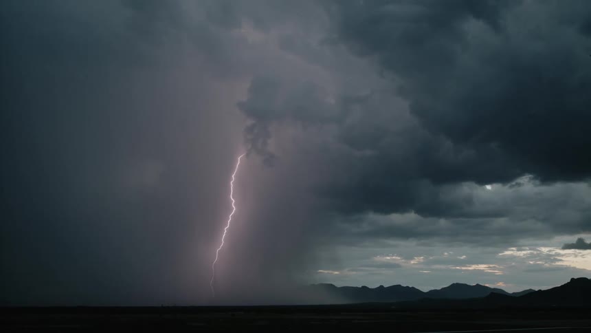 Lightning storm falling on flat ground with mountains on horizon