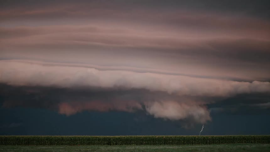 A lightning falling from a huge black cloud onto an empty field