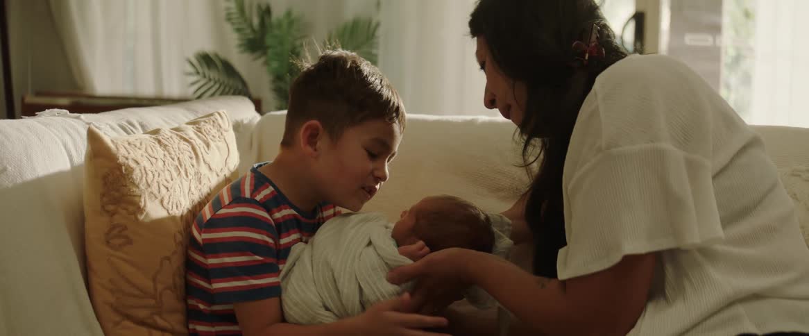 A woman with a baby in her arms while a child kisses and cuddles the baby