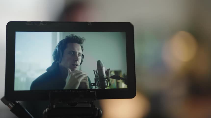 Close up of a man on a video screen wearing headphones and talking into a microphone while conversing with someone else