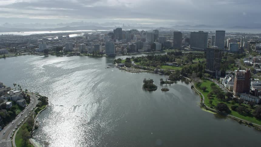 Aerial tilt from residential neighborhoods to reveal and fly over Lake Merritt towards downtown Oakland showcasing the urban landscape of this northern California city on a partly cloudy day