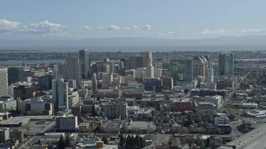 A stunningaerial footage of flying past downtown office buildings in Oakland California showcasing the bustling city skyscrapers and bustling streets during a partly cloudy day
