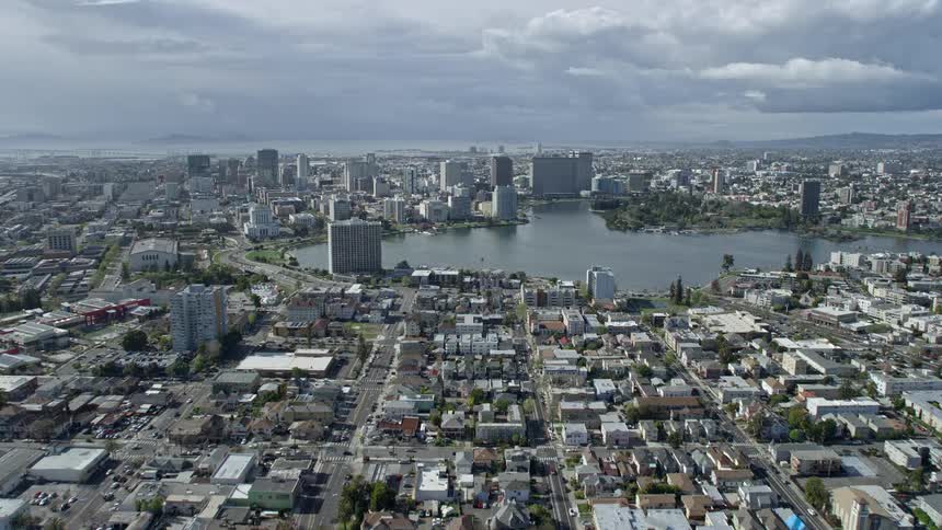  aerial footage showcasing the approach towards Lake Merritt and Downtown Oakland in California with a wide-angle view capturing the city's skyline the partially cloudy skies and the beautiful lake in the center of the bustling metropolis