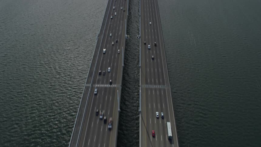  aerial tilt footage showcasing a wider view of the Bay Bridge in Oakland California during daylight with cloudy skies and light traffic