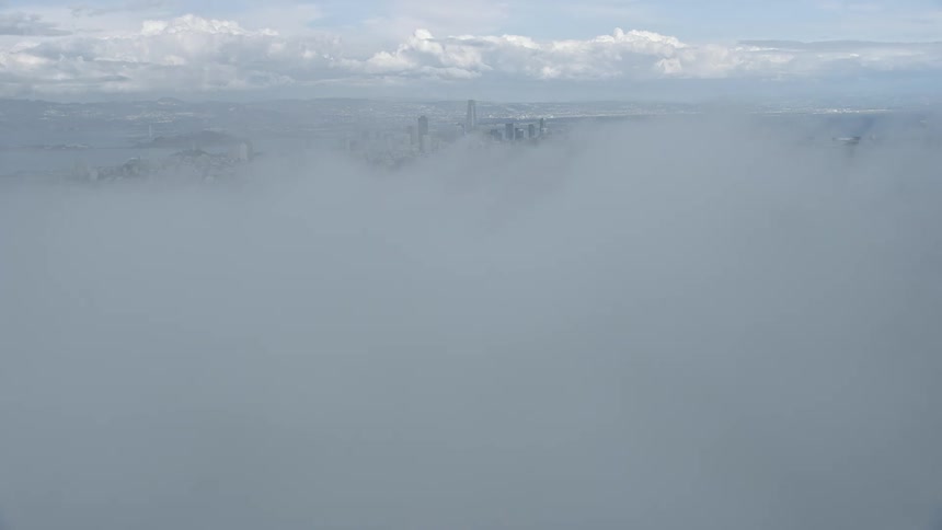  aerial footage showcasing the stunning San Francisco skyline emerging from a sea of fog offering an view of the city's high-rises and downtown area on a beautiful partly cloudy day in California's Bay Area