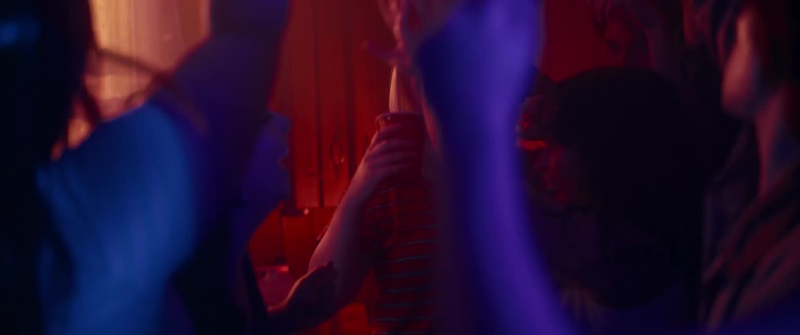 A group of people dancing around in a dim lit room holding drinking cups while laughing and smiling