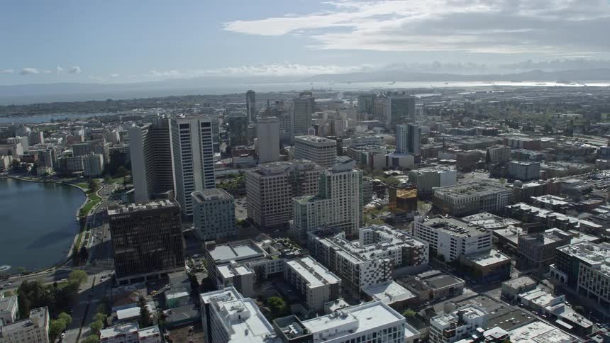  aerial footage of downtown office buildings in Oakland California captured during a partly cloudy day with an orbiting camera showcasing the bustling city and industrial area in the Bay Area of northern California