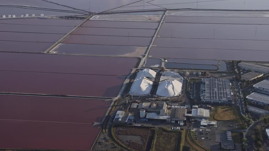 Aerial footage of salt mounds and marshes in Newark California showcasing the industrial manufacturing of salt with partly cloudy skies