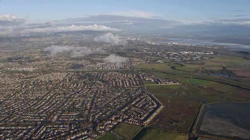 Aerial footage of wide suburban neighborhoods in Union City California showcasing the coastal view and the separation from fields on a foggy day shot during the summer in the Bay Area