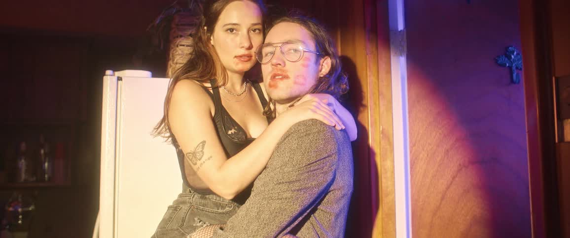 A couple kissing in a dark room are surprised when a light shines in their direction