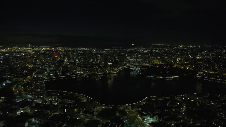 Aerial footage of downtown Oakland and Lake Merritt at night in California showcasing the lit-up city surrounding a small body of water