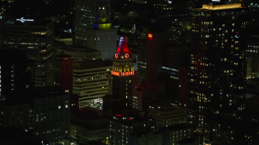 Aerial footage of Tribune Tower in Downtown Oakland at night showcasing red lights flashing atop the tower in a metropolis