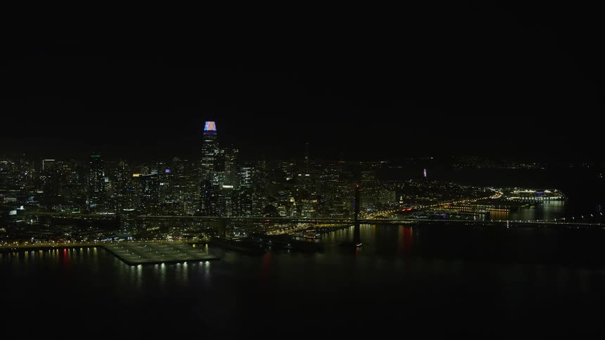  aerial footage capturing a stunning reverse view of the Bay Bridge and downtown San Francisco skyline at night in Northern California with clear skies and a captivating cityscape