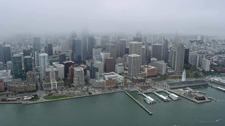 Aerial flyover of Bay Bridge towards Downtown San Francisco skyline on a foggy day capturing the high rises and skyscrapers of the city