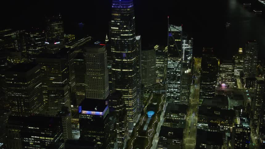 aerial footage of Salesforce Tower orbiting the city skyline at night in Downtown San Francisco showcasing the modern buildings and skyscrapers under clear skies in Northern California