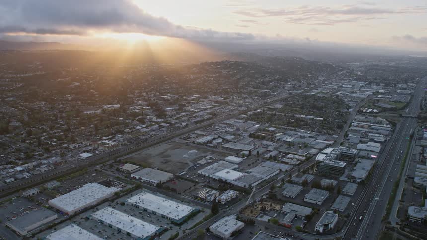  aerial footage capturing the breathtaking sunset view as the camera glides over warehouse buildings towards picturesque hillside homes in San Carlos California