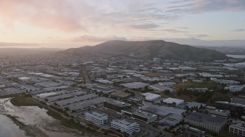 Approaching South San Francisco office and warehouse buildings at sunset with partly cloudy skies and a wide-angle view in thisaerial clip shot over the San Francisco Peninsula using a Shotover F1 onHelium camera