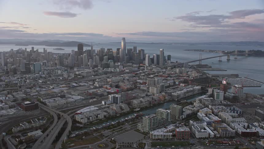  aerial footage capturing the approach towards San Francisco's iconic skyline at sunset as seen from South of Market showcasing the high-rise buildings and cityscape in Northern California