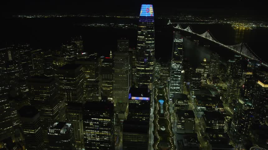 Aerial footage of Salesforce Tower at night as an approach and flyby over Downtown San Francisco with clear skies and views of the Bay Bridge and the city's skyscrapers