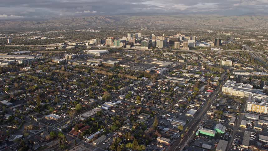  aerial footage capturing an sunset view of Downtown San Jose California as the camera tilts up from urban homes revealing the city's vibrant downtown area and hazy neighborhoods at dusk