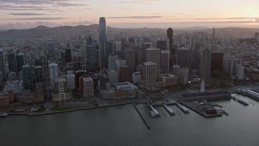  aerial footage of Downtown San Francisco at sunset showcasing the high rises and skyscrapers with partly cloudy skies in the background captured using a Shotover F1 camera giving a stunning side view of the city's downtown area during the spring/summer s