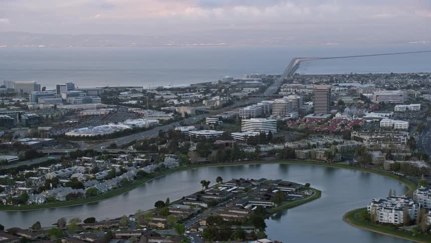  aerial footage of office buildings near the San Mateo Bridge at sunset in Foster City California showcasing the industrial landscape with partly cloudy skies and a picturesque view of the bay area in northern California