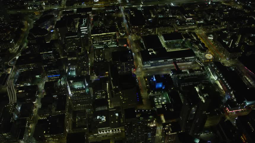 anaerial footage capturing office buildings and the iconic Moscone Center illuminated at night in downtown San Francisco California showcasing the city's vibrant nightlife and its bustling commercial and convention district