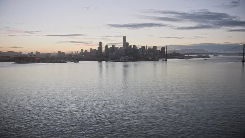  aerial footage capturing the picturesque view of the Downtown San Francisco skyline at twilight showcasing the high rise buildings cityscape and the Bay Bridge shotover with low flying altitude over the San Francisco Bay area during the summer season