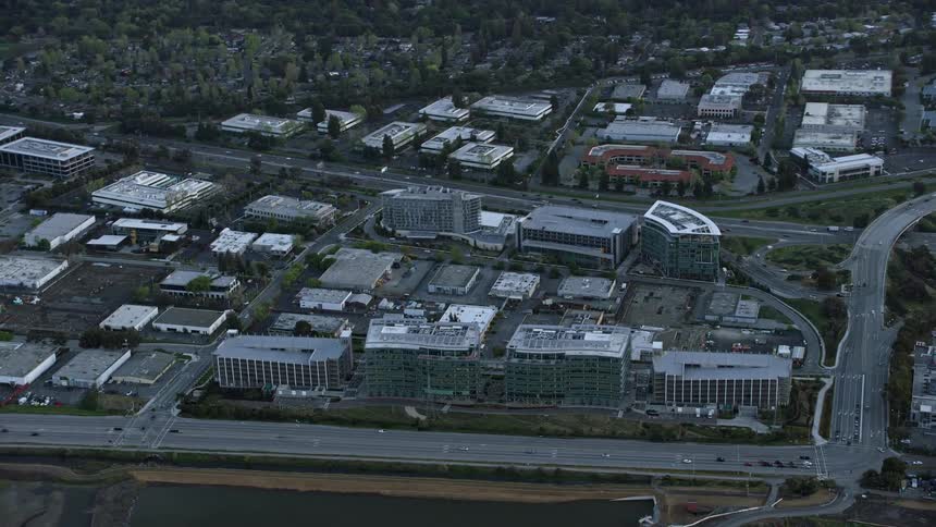  aerial footage of Facebook office buildings at sunset in Menlo Park California showcasing the modern buildings and surrounding roads with partly cloudy skies adding to the epic industrial atmosphere of the shot