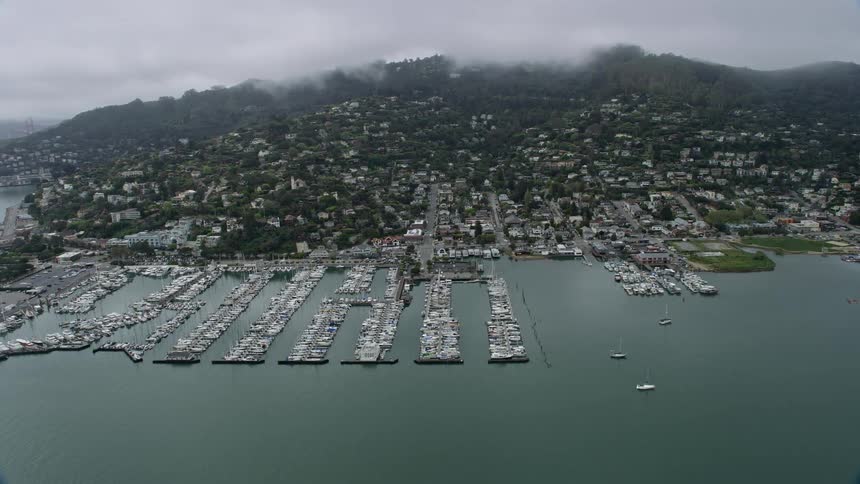 Aerial footage of foggy coastal neighborhoods and marinas in Sausalito California showcasing the charm of the marinas nestled within the scenic coastal town