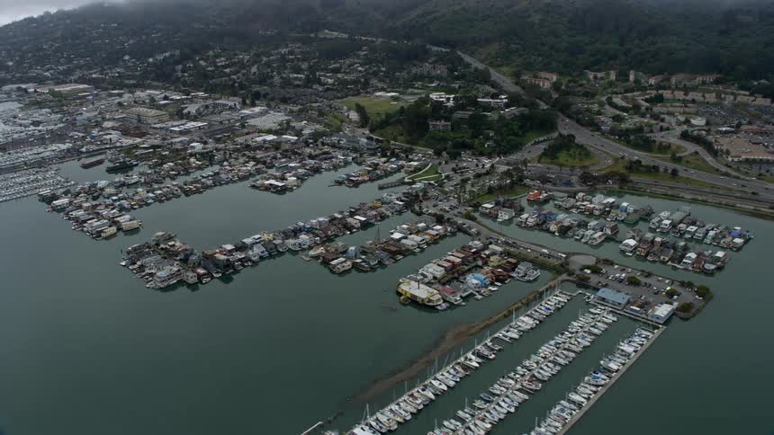  aerial footage of houseboats docked at Sausalito harbor on a foggy day in California showcasing the coastal community surrounded by overcast skies and the scenic view of the San Francisco Bay