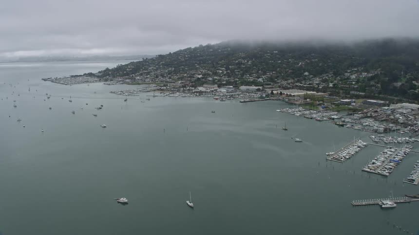 Aerial footage of foggy day flying over Sausalito neighborhoods and marinas showcasing seaside residential areas boatyards docks and the marina on the shoreline of San Francisco Bay in the Bay Area California