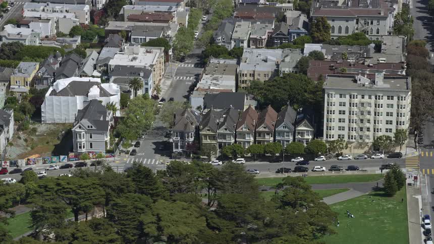  aerial footage showcasing the iconic Painted Ladies Victorian homes in San Francisco's Western Addition neighborhood with a side view of the residences and the surrounding sunny cityscape