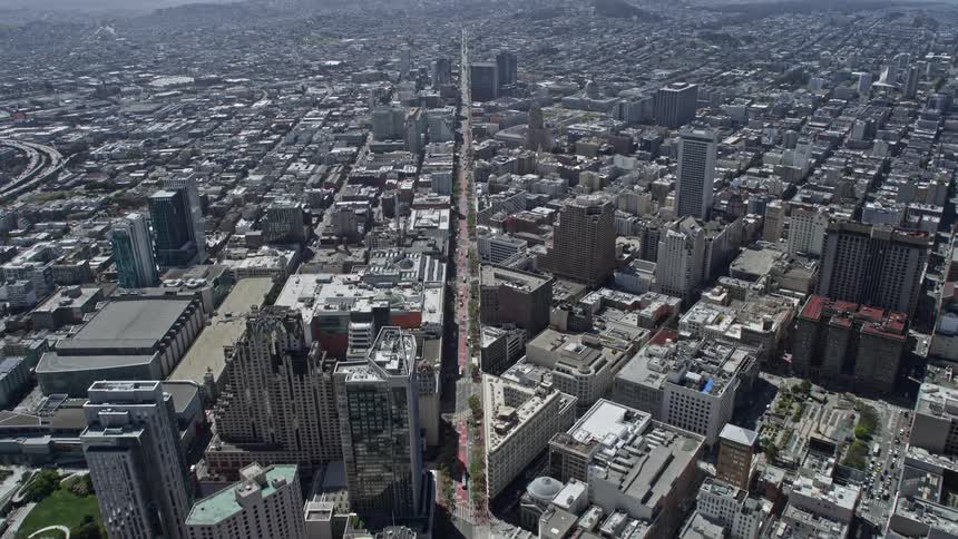 Aerial footage flying over downtown San Francisco's Market Street towards Civic Center capturing the city's high-rise buildings city streets and partly cloudy skies