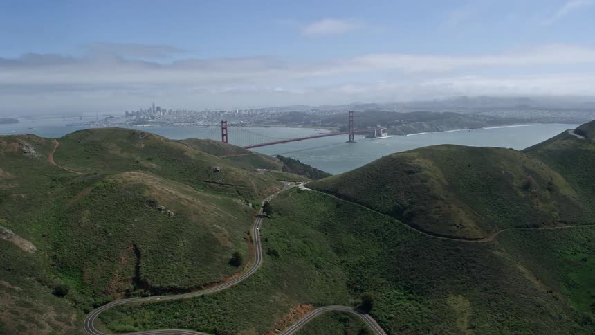 Aerial view of the Golden Gate Bridge from the Marin hills offering wide angle shot of the iconic structure in San Francisco California with partly cloudy skies and city view in the distance shot during daytime in the Bay Area