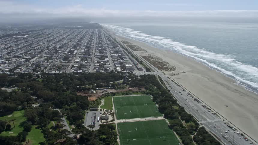  aerial footage of flying over Golden Gate Park and beach towards Outer Sunset San Francisco showcasing the picturesque city park shoreline and residential areas with partly cloudy skies and an empty beach in the outer sunset district during spring/summer