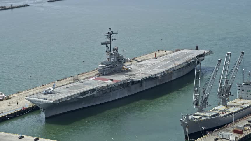  aerial footage of an aircraft carrier docked in Alameda California showcasing naval ships and vessels in the port on a cloudy day