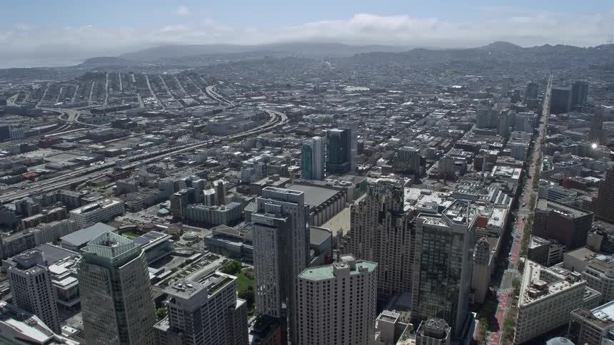 an aerial view of Downtown San Francisco skyscrapers and buildings surrounded by sunny California sunshine as the camera flies over the city towards South of Market