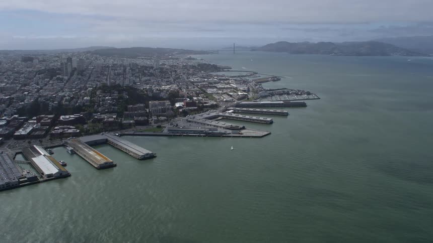 Aerial footage of Coit Tower and North Beach piers in San Francisco California showcasing the city's historic landmarks and waterfront during a cloudy day