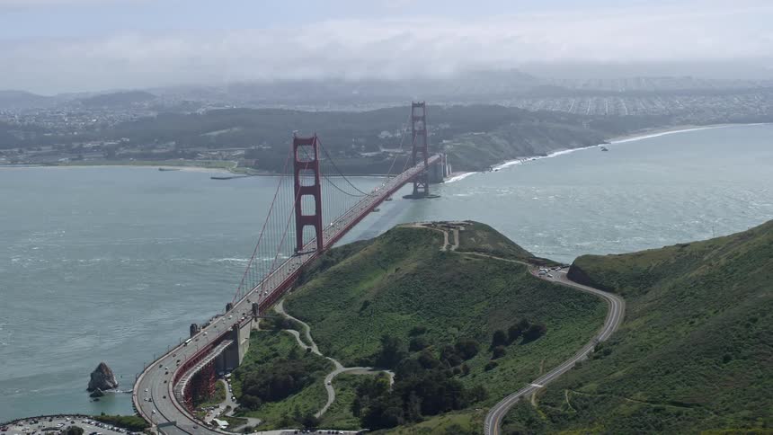  aerial footage of the iconic Golden Gate Bridge viewed from the Marin hills on a partly cloudy day showcasing the transportation hub and historic landmark in San Francisco California
