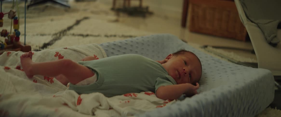 A very young baby lays on its back while wiggling and looking around