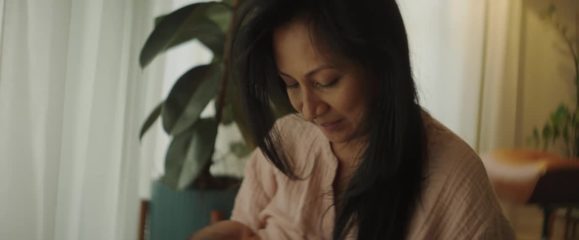 A woman breastfeeds an infant while sitting in a living room