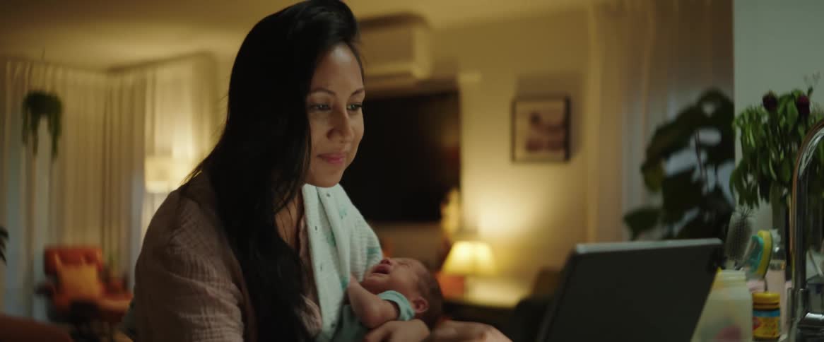 Mother holds a baby while using a laptop at home