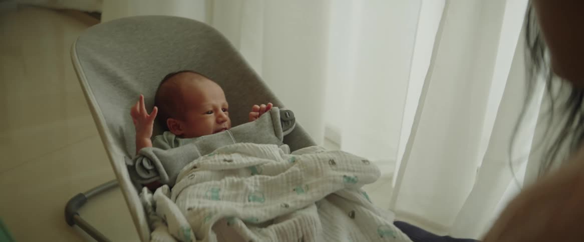 A mother covering a newborn baby who is rocking in a baby chair