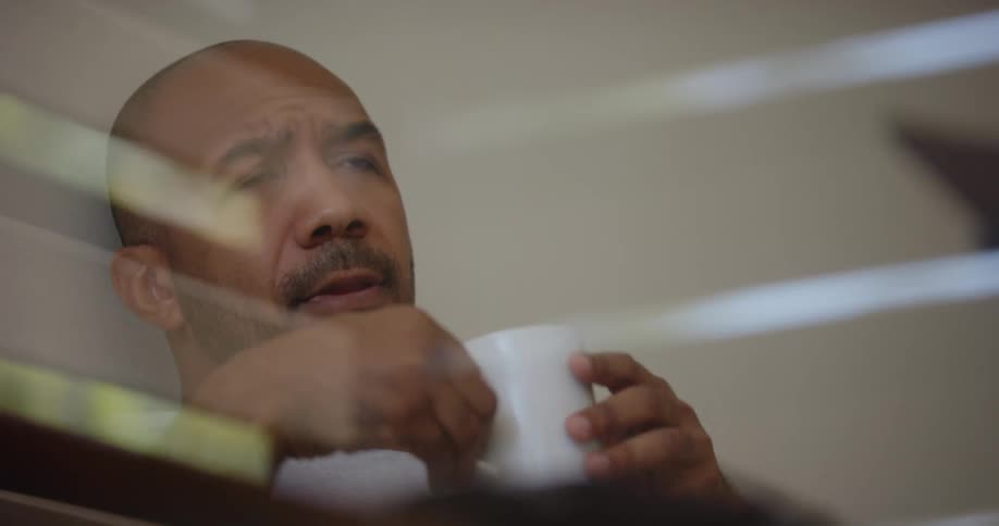Man lying in bed drinking coffee from a white cup