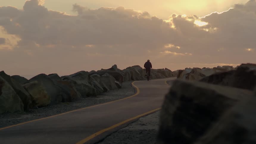 A man rides his bicycle down a paved path through a canyon