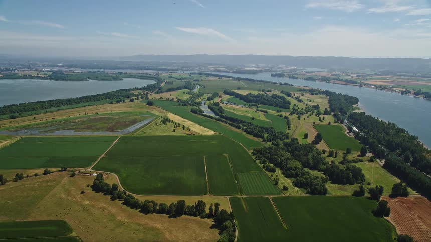 aerial footage showcasing the scenic rural countryside filled with farms and green fields near the Columbia River in Vancouver Washington on a sunny day